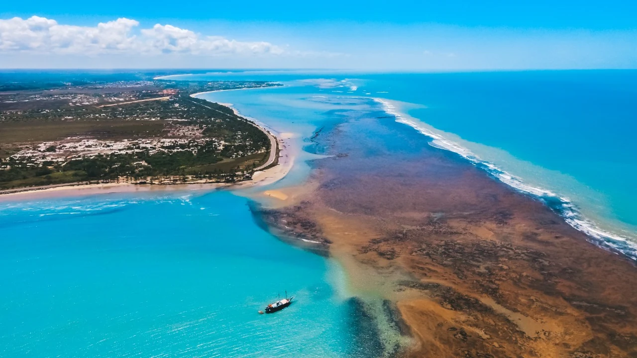 Vista aérea de Ponta Grande, com a praia, a bancada de corais e uma embarcação ao largo